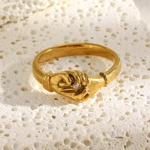 Gros plan d'une bague mains entrelacées en acier doré avec diamant sur pierre blanche