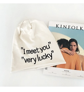 Dettaglio del berretto in maglia crema con ricamo I meet you very lucky e rivista Kinfolk