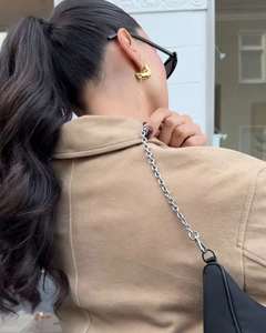 Détail de boucles d'oreilles dorées et sac à bandoulière noir avec chaîne argentée
