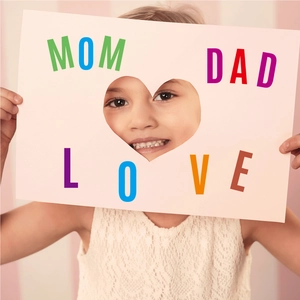 Close-up of a child holding heart-shaped cutout card with MOM DAD LOVE letter stickers