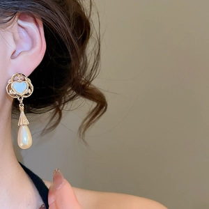 Close-up of vintage heart stud earring with large teardrop pearl on model's ear