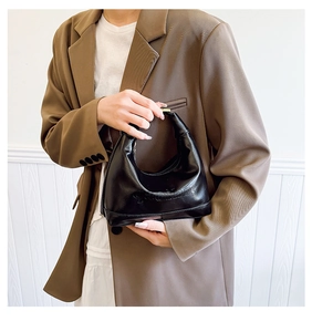 Close-up of black PU leather pillow bag featuring gold metal handle and embossed details