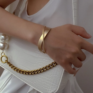 Matte gold double-layer crisscross open bangle bracelet on a white textured background
