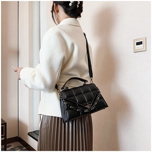 Detail view of a black quilted handbag with a gold chain strap worn by a woman