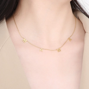 Close-up of golden MAMA letter pendants necklace on model in beige blazer outfit