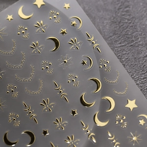 Golden bronzing nail art stickers with celestial star and moon patterns on grey background