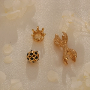 Detailed view of gold crown charm, bicolor beads, and claw pendant on beige fabric