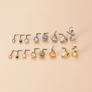 Variety of stainless steel L-shaped nose studs with opal and heart accents on beige background