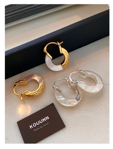 Detailed close-up of metallic C-shaped earrings with mother of pearl and Confession engraving