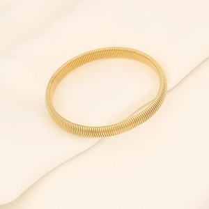 Detailed view of golden elastic spring-style bangle on white textured silk fabric