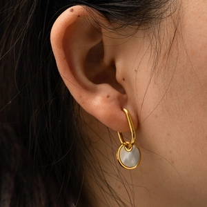 Titanium steel gold hoop earrings featuring a white round shell pendant on model