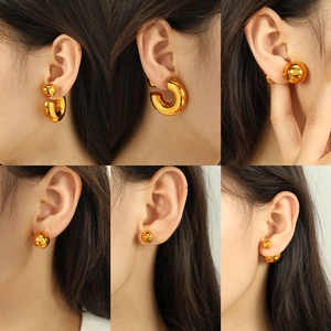 Polished gold hollow C-shaped hoop earrings and sphere studs on model ear