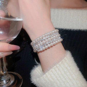 Detail view of multilayer pearl and diamond bracelet worn while holding a wine glass
