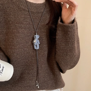 Détail du collier ours en tissu avec strass et corde marron sur un pull d'hiver