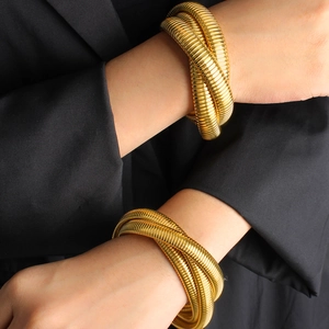 Three-layer stretch snake chain bracelet in gold finish worn on wrist with dark blazer