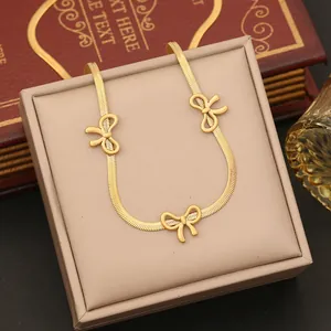 Detail of a gold snake chain necklace with bow pendants inside a jewelry box