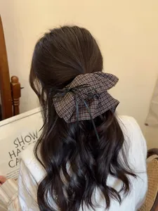 Detail of a large brown plaid bow hair clip with black ribbons worn on a half-up hairstyle