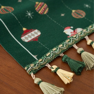 Green Christmas table runner with festive jacquard patterns and tassel detail on wood surface