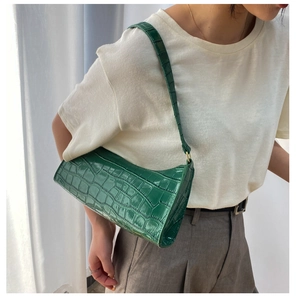 Detalle del bolso baguette verde oscuro con textura de cocodrilo y hebillas doradas