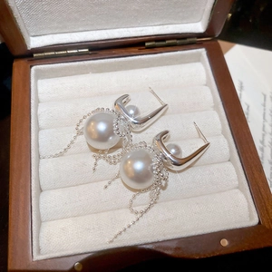 Detailed close-up of pearl bow earrings with silver tassel chains in a wooden box