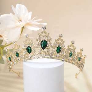 Detailed macro of gold baroque crown featuring green teardrop gems and white rhinestones