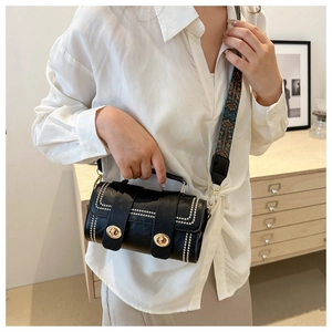 Detail of black cylindrical handbag with golden clasp and ethnic patterned wide strap