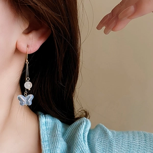 Detailed close-up of a blue butterfly earring with white bead on a golden hook