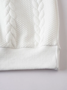 Detail of white knitted sweater featuring cable knit texture and ribbed hem detail
