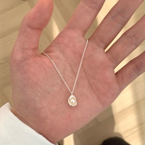 Macro shot of 925 silver necklace with white pearl pendant held by hand on wood background