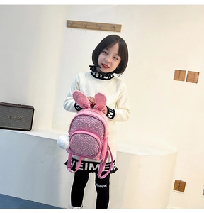 Pink sequin toddler backpack with cute bunny ears and plush ball charm on a girl