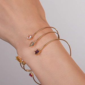 Détail de joncs ouverts en plaqué or avec zircons colorés superposés sur un poignet féminin