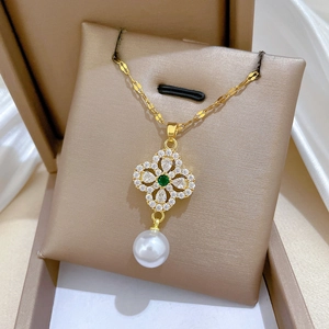 Detail of gold flower necklace with green gemstone, diamond accents and hanging pearl