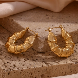 Detail of 18K gold plated hollow tire hoop earring displayed on natural stone and silk