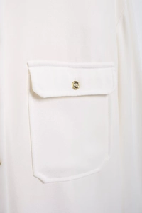 Detail of white crepe blouse pocket with flap and decorative gold metallic button