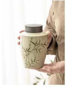 Hand holding ceramic tea canister with bamboo patterns and alloy lid in soft sunlight