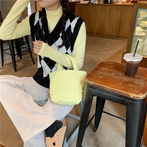 Close-up of a pale yellow quilted cotton mini bag carried by a model in a cafe