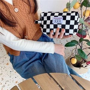 Détail d'une trousse de maquillage à carreaux en velours côtelé tenue à la main