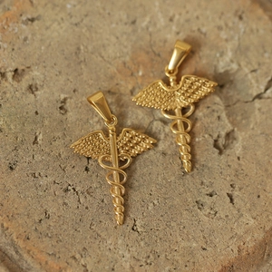 Detailed view of two gold-plated titanium Caduceus pendants on a natural stone surface