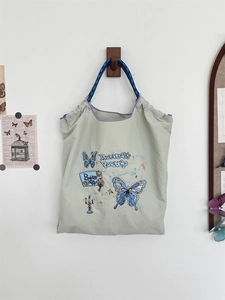 Detail of light green tote bag with blue butterfly embroidery and woven rope handles