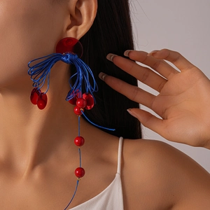 Close-up of long bohemian earrings with red acrylic discs and blue knotted rope tassels