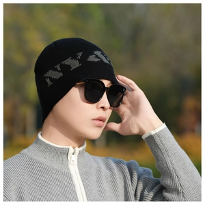 Outdoor shot of a thick black knit beanie with grey lettering on a male model