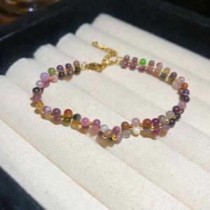 Close-up of tourmaline beaded bracelet with gold chain and heart pendant on velvet display