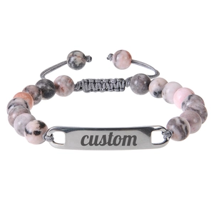 Detailed macro view of custom engraved metal plate on pink zebra stone beaded bracelet