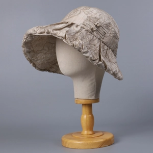 Detail of beige sun hat with brown vine patterns and ruffled brim on a model stand