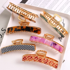 Detail of six large hair claws with acetate patterns and gold metal frames on a tray