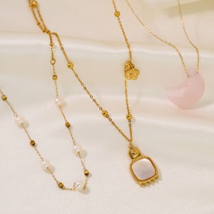 Detailed shot of 14K gold necklaces with white shell flower and pearl charms on silk