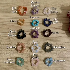 Flat lay of 15 various natural gemstone chip stretch rings on a light wood texture surface
