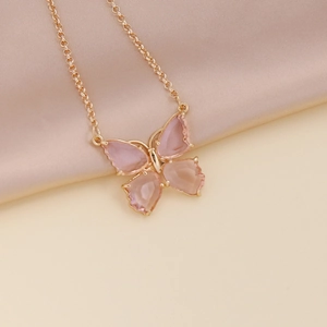 Close-up of pink butterfly pendant with gold chain on soft pink silk background