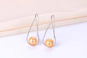 Detailed shot of drop-shaped orange pearl earrings with silver wire frames on white fabric