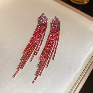 Detailed macro view of cascading red rhinestone tassel earrings on beige satin background